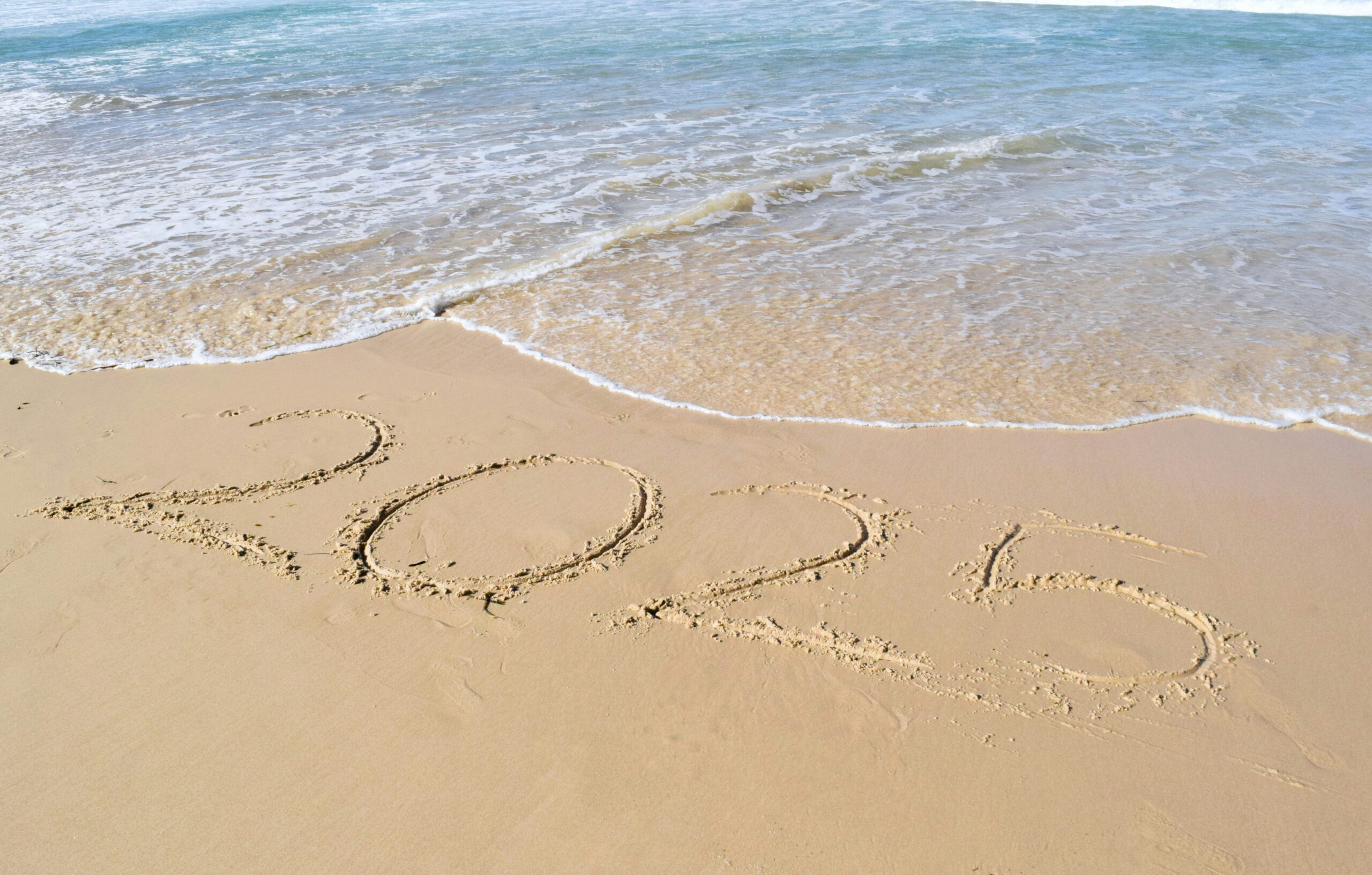 A sandy beach with "2025" written in the sand